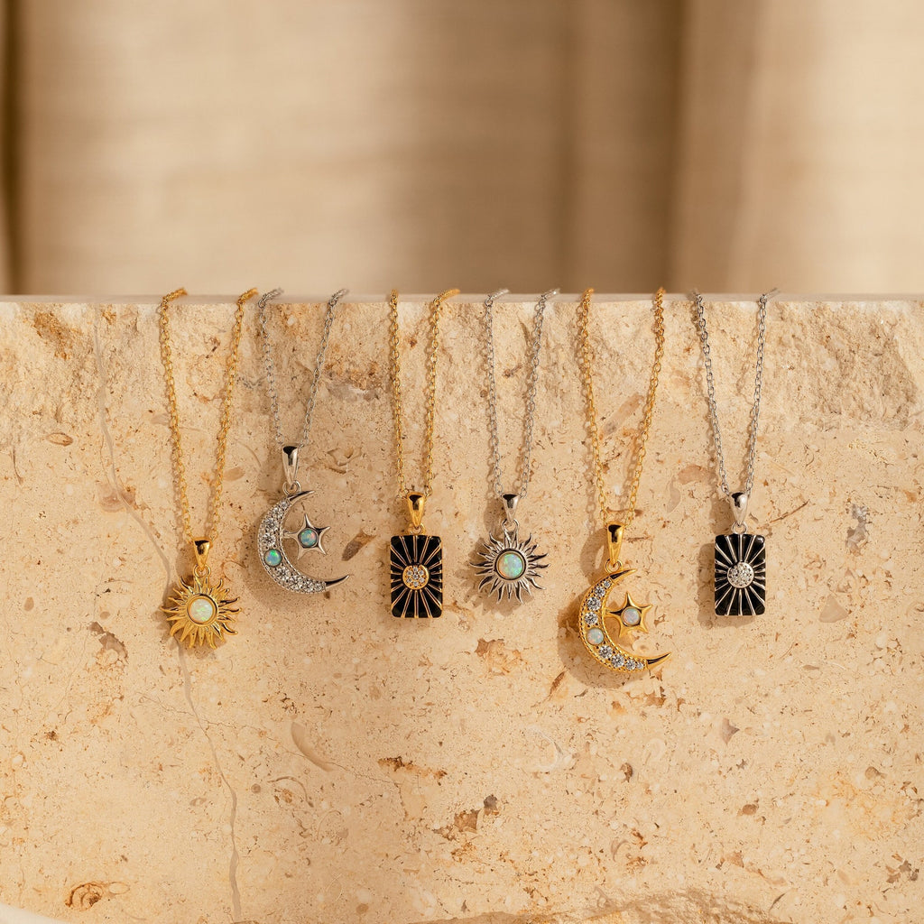 Six gold and silver Celestial Pendant Necklace Set pieces with sun, moon, and star charms—some featuring opal and diamond accents—are arranged on a beige stone surface. A perfect gift for her, inspired by the beauty of the night sky.