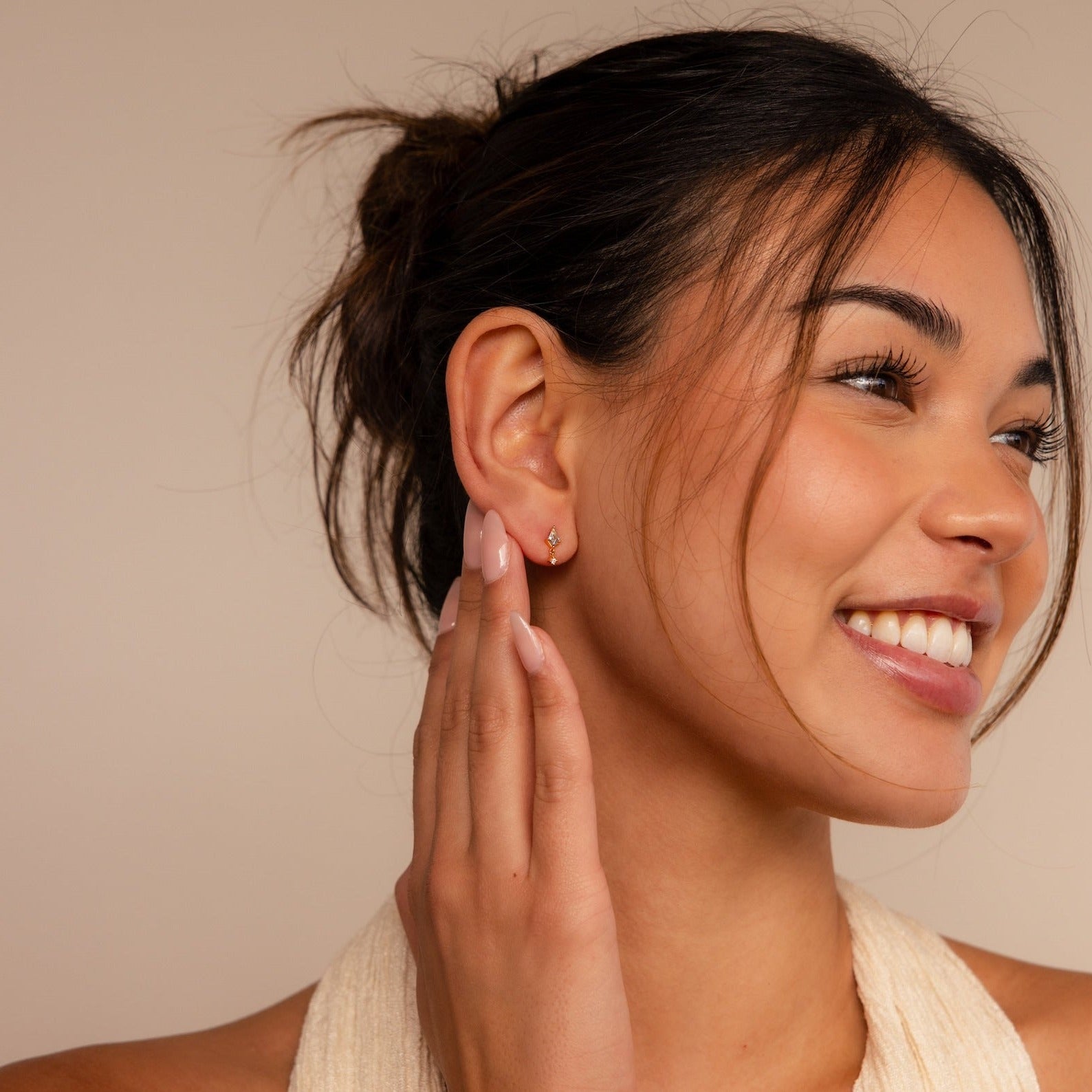 A smiling woman with tied-back hair touches her ear, highlighting the Aquamarine Kite Drop Earrings in a subtle geometric design against a beige background.