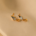 Aquamarine Kite Drop Earrings with diamond-shaped blue CZ gemstones and small square accents on gold studs, displayed on a beige background.