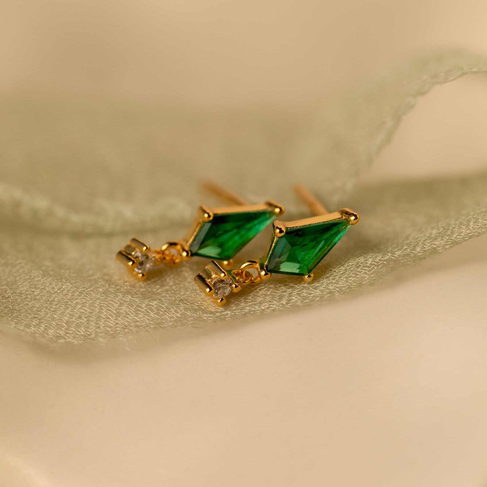 Emerald Kite Drop Earrings with sparkling CZ diamond accents, elegantly displayed on soft light green fabric—an ideal touch of luxury for your jewelry collection.