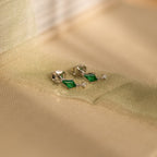 Emerald Kite Drop Earrings rest elegantly on a fabric surface, highlighting the brilliance of CZ Diamond craftsmanship and refined jewelry design.