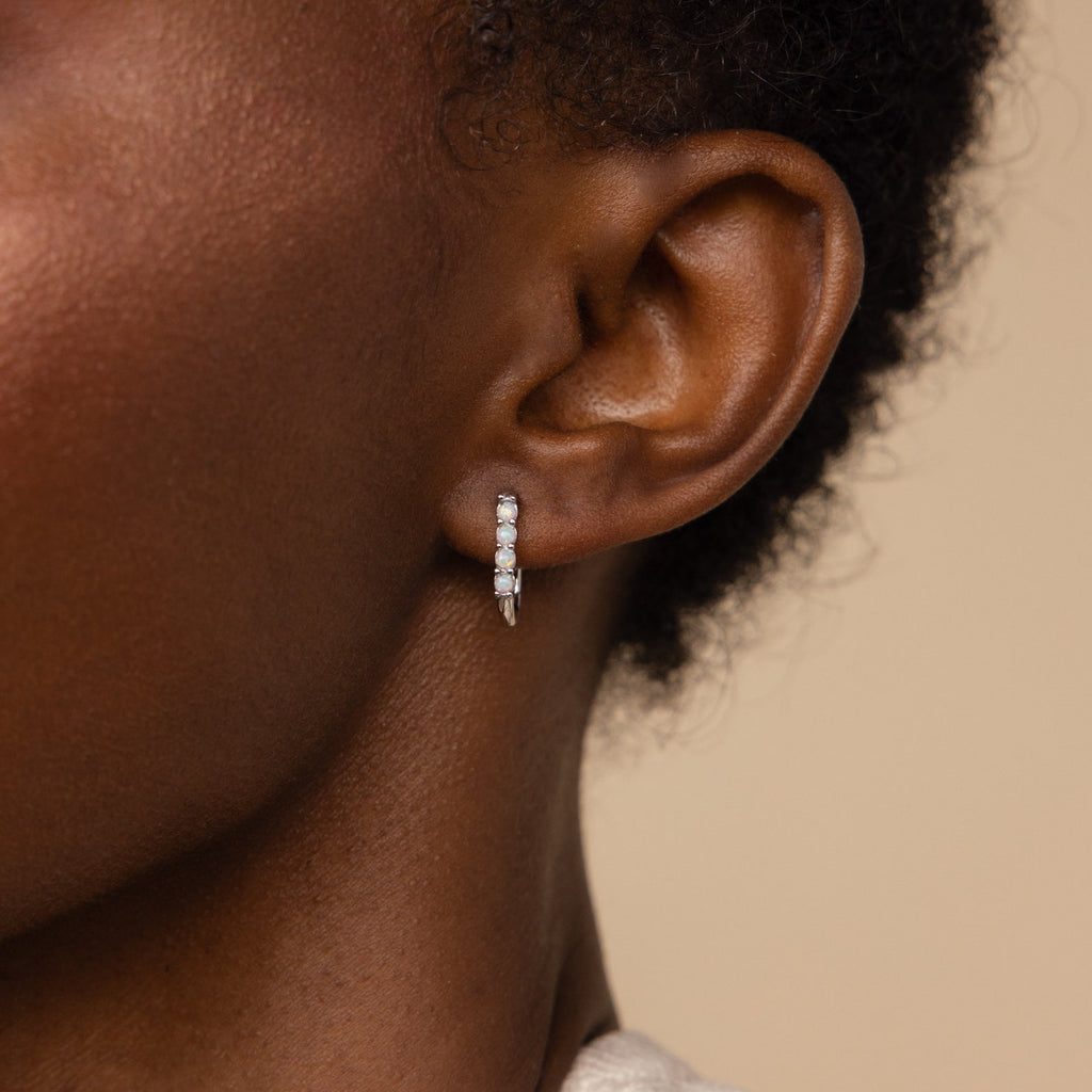 Close-up of a person's ear wearing Opal Link Hoops—small silver hoop earrings featuring sparkling stones and an opal link design.