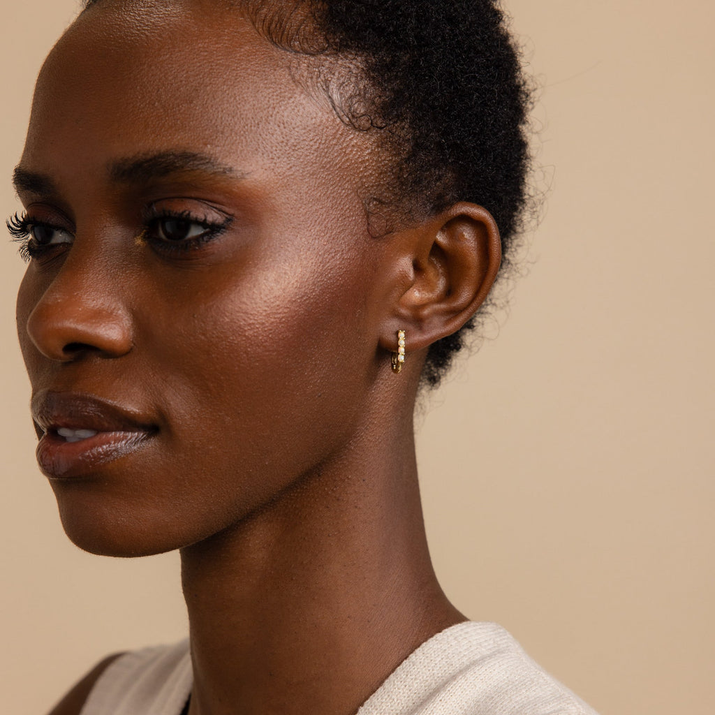 A woman with short curly hair wears the Opal Link Hoops and a sleeveless top, facing left against a beige background.