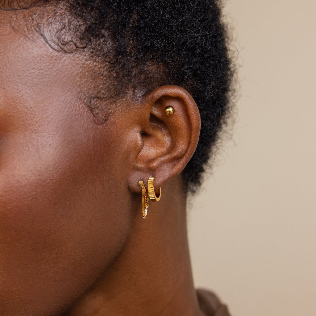 Close-up of a person’s ear with a stylish earring stack: a stud, two small hoops, and the elegant Flatback Chain Earrings in gold.