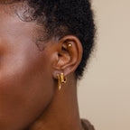 Close-up of a person’s ear with a stylish earring stack: a stud, two small hoops, and the elegant Flatback Chain Earrings in gold.