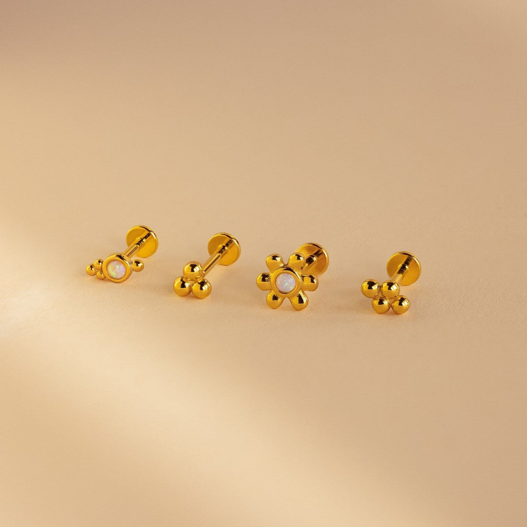 The Opal Cluster Studs Set features four gold flower earrings, two with pearl centers, displayed on a beige background—ideal for cartilage piercings or as elegant accents paired with opal cluster studs.