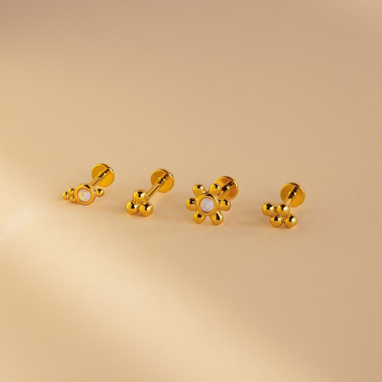 The Opal Cluster Studs Set features four gold flower earrings, two with pearl centers, displayed on a beige background—ideal for cartilage piercings or as elegant accents paired with opal cluster studs.