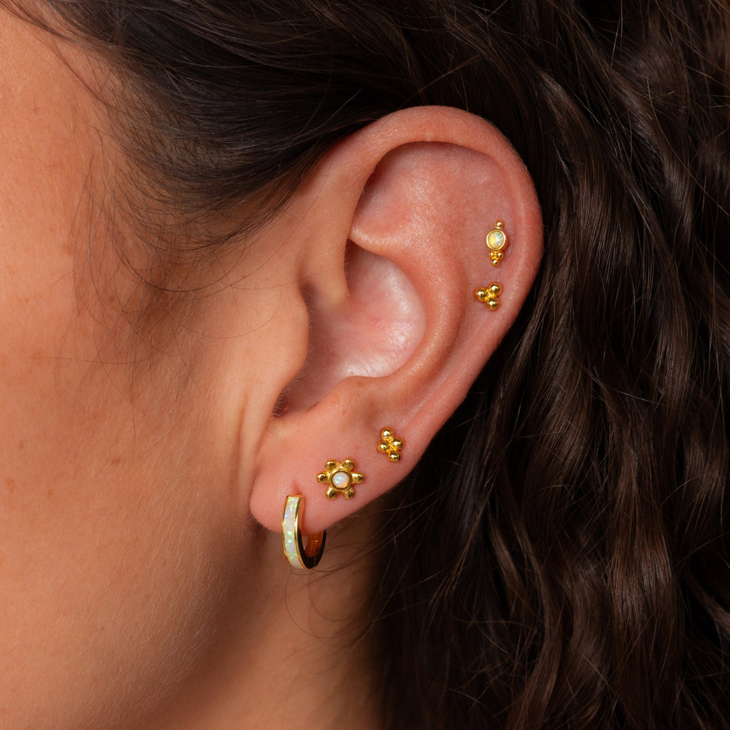 A close-up of an ear with multiple gold cartilage piercings, featuring the Opal Cluster Studs Set, and wavy brown hair visible.