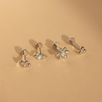 The Opal Cluster Studs Set includes four silver stud earrings with flower and paw designs, displayed on a beige surface—ideal accents for cartilage piercings.