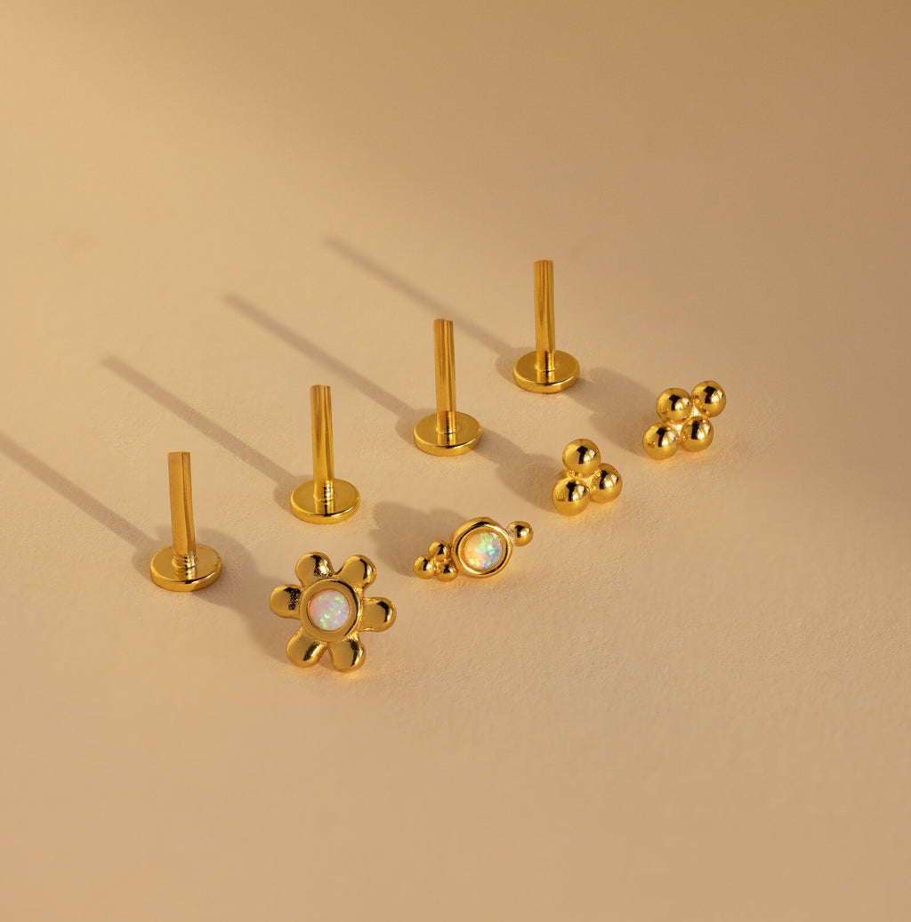 The Opal Cluster Studs Set includes five gold earrings with unique shapes, perfect for cartilage piercings, featuring floral and beaded designs, all displayed on a beige background.