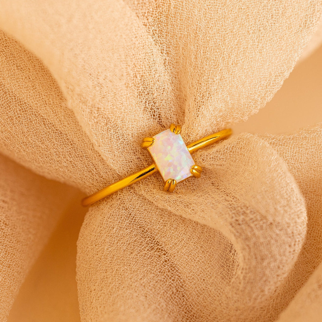 Opal Emerald Ring featuring a rectangular opal gemstone, elegantly presented on peach-colored fabric—an exquisite anniversary gift or unique engagement ring.