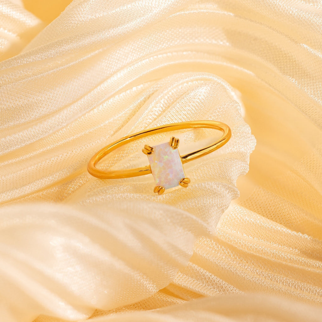 The Opal Emerald Ring, featuring a rectangular opal stone, rests on soft cream satin fabric—an elegant anniversary gift.