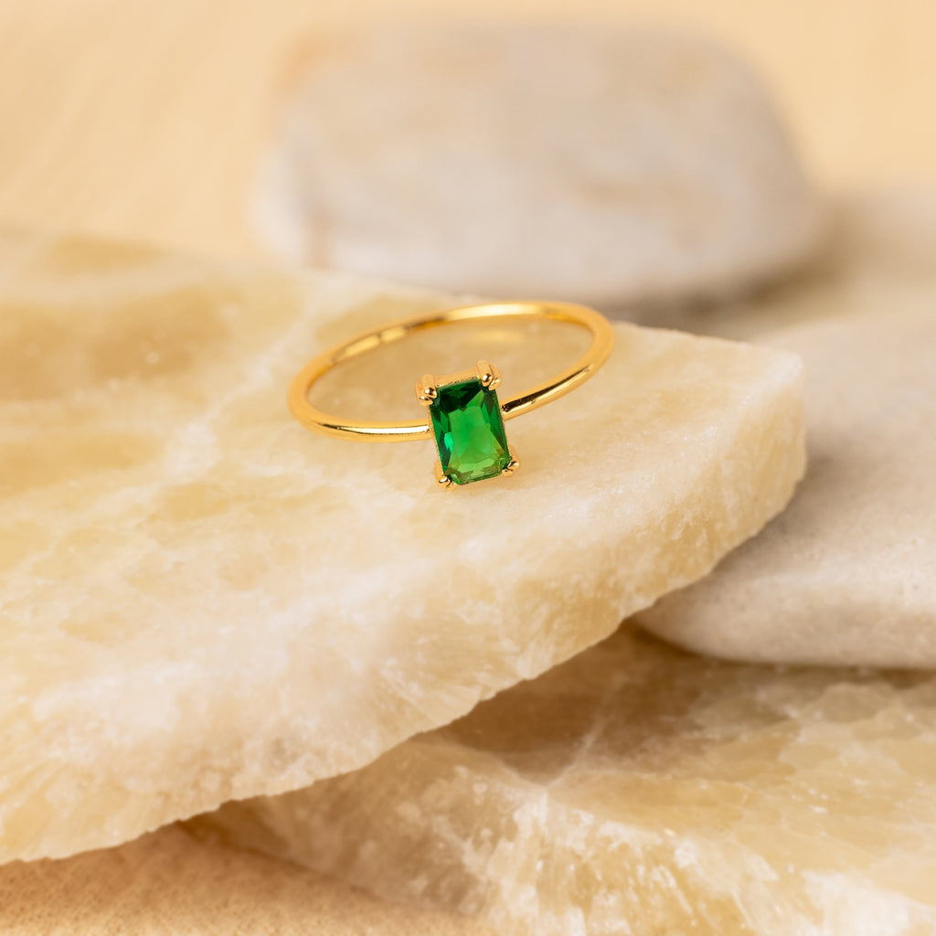 Harley Emerald Ring - Silver: This vintage-inspired silver ring showcases a rectangular green gemstone, beautifully displayed on light-colored stone slabs.