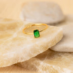 Harley Emerald Ring - Silver: This vintage-inspired silver ring showcases a rectangular green gemstone, beautifully displayed on light-colored stone slabs.