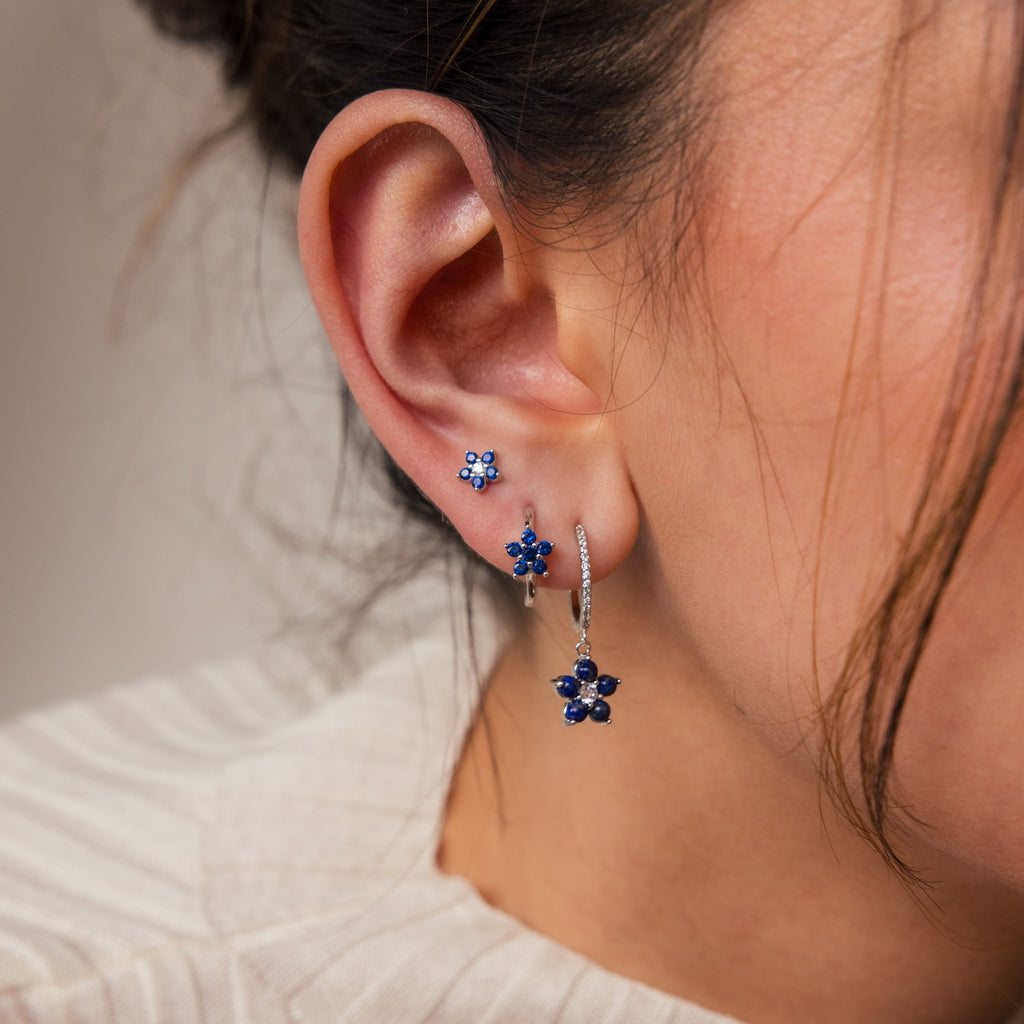 Close-up of a woman's ear wearing the Sapphire Flower Earrings Set, a stunning addition to any jewelry collection, paired with a cream-colored top.