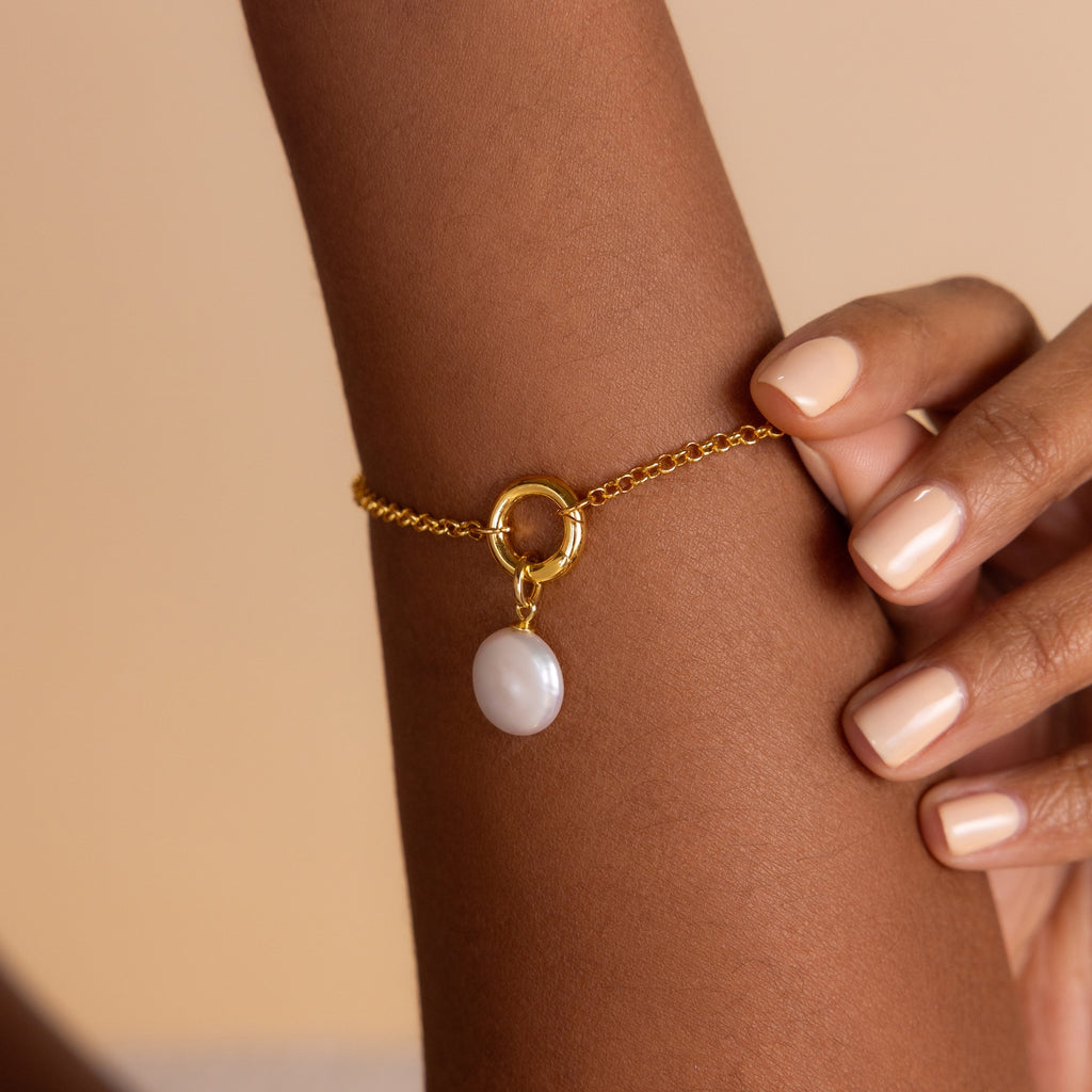 The Rolo Circle Charm Bracelet, featuring a round pearl charm, adds elegance to a wrist with nude-painted nails. Its detachable hinged circle lets you personalize your look with additional charms.