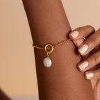 The Rolo Circle Charm Bracelet, featuring a round pearl charm, adds elegance to a wrist with nude-painted nails. Its detachable hinged circle lets you personalize your look with additional charms.