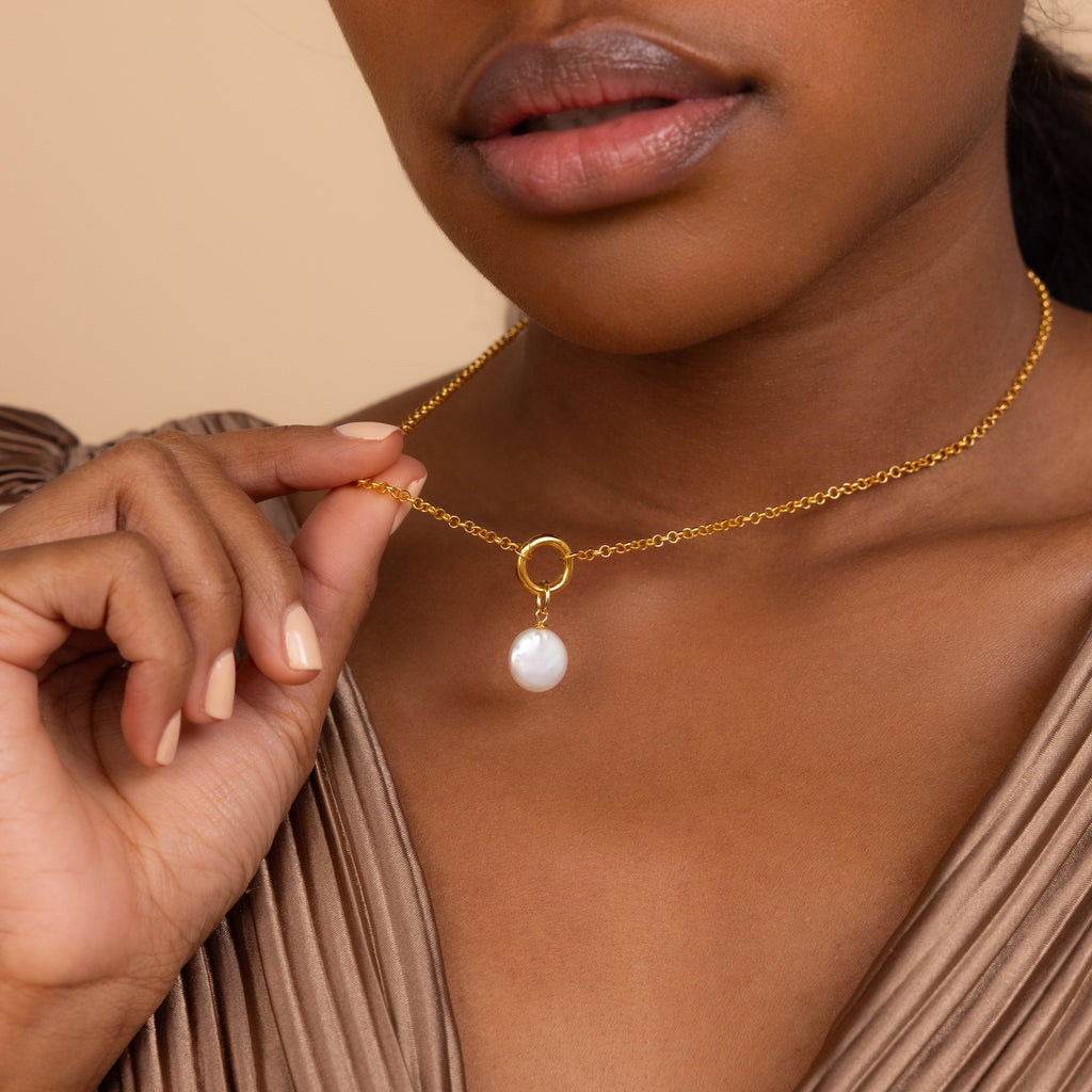 A woman delicately holds the Round Pearl Charm gold chain necklace near her neck.