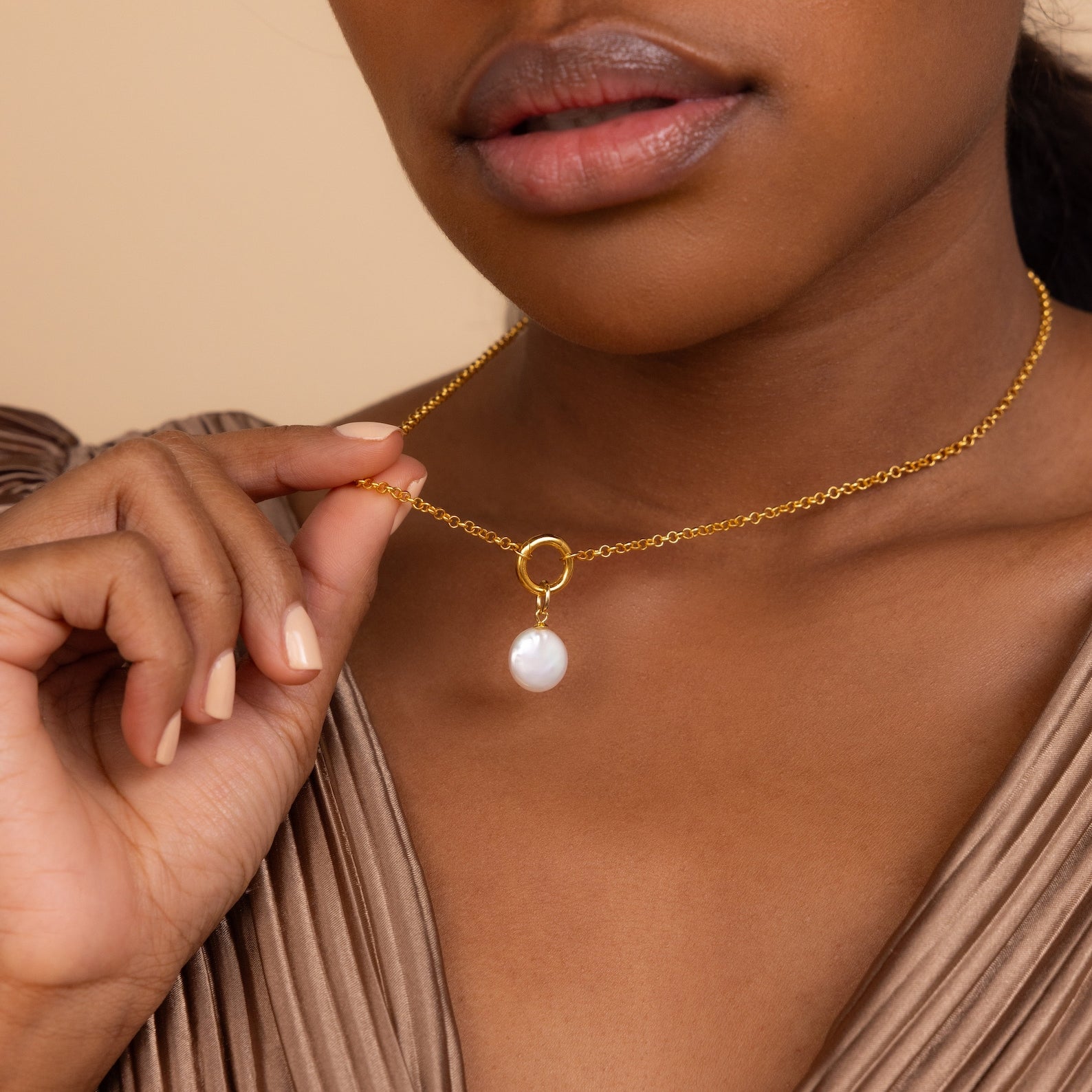 A woman delicately holds the Round Pearl Charm gold chain necklace near her neck.