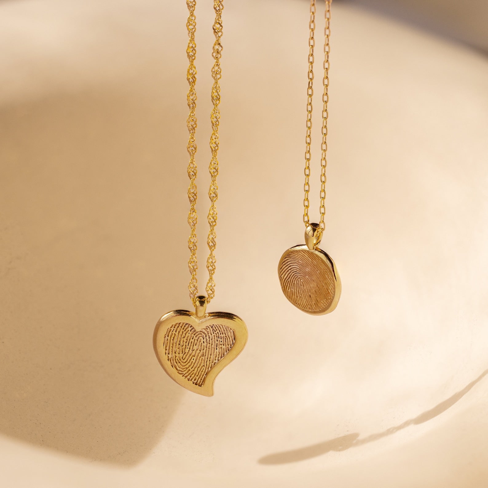 The Fingerprint Heart Necklace, a gold pendant resting on a neutral background, offers a meaningful gift idea for Mother's Day or as a memorial keepsake.