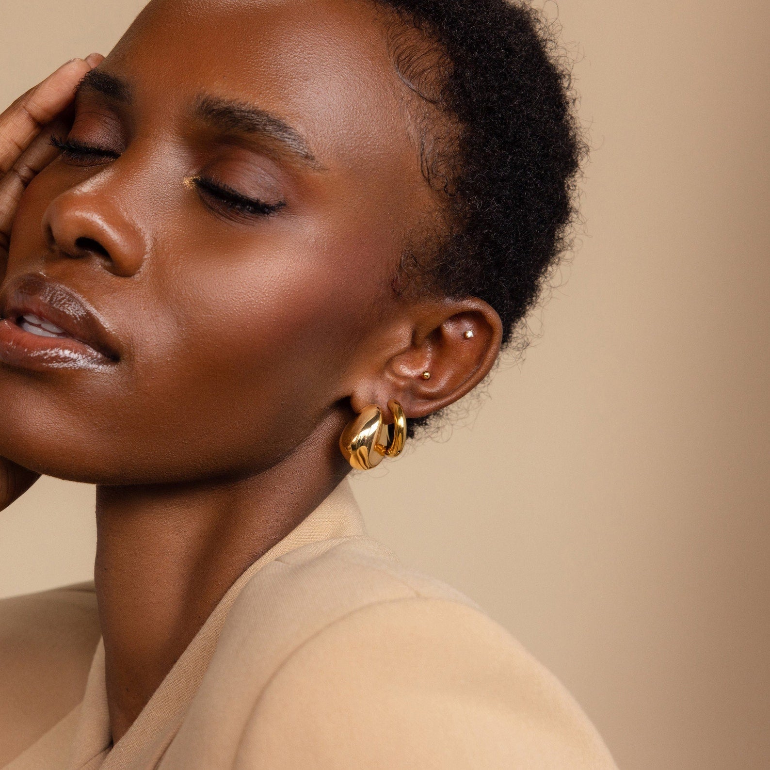 A woman with short hair and closed eyes poses gracefully, gently touching her face while wearing Bold Teardrop Studs.