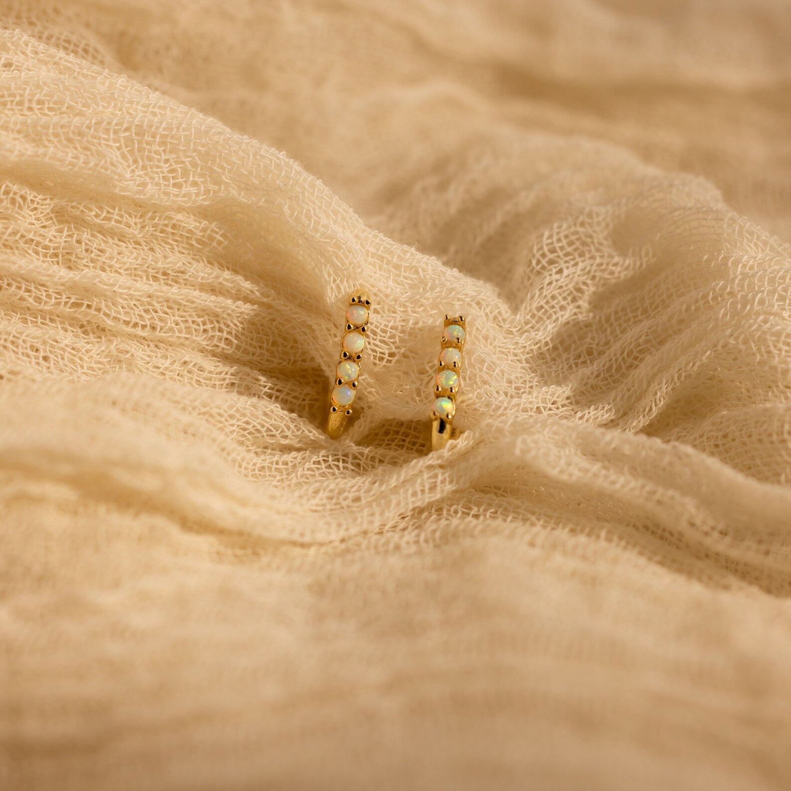 Opal Link Hoops: Gold hoop earrings featuring small white beads, inspired by elegant opal designs, shown on textured beige fabric.