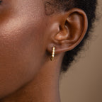 Close-up of a person's ear wearing the Opal Link Hoops, featuring small gold hoops adorned with shimmering white opals.