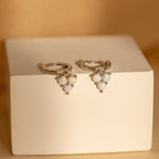 Opal Cluster Huggies with small iridescent opals rest on a beige block—these dainty hoop earrings are a perfect bridesmaid gift.