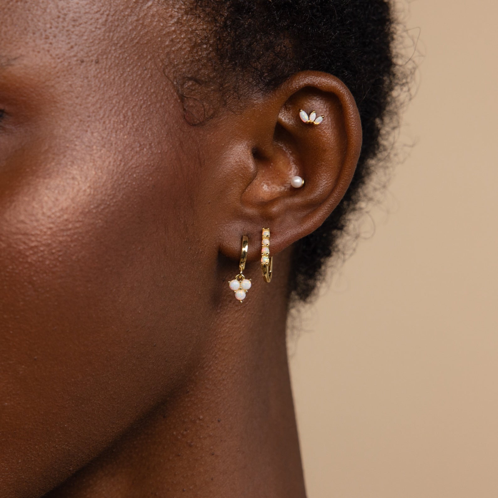 Close-up of an ear adorned with gold, pearl, and dainty hoops, highlighting Opal Cluster Huggies against a neutral background—an ideal bridesmaid gift.