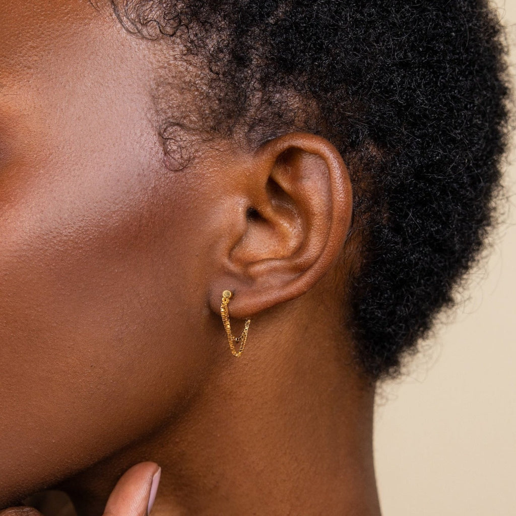 Close-up of a person with short curly hair wearing the Flatback Chain Earrings—minimalist gold hoops with chain details—ideal for an elegant earring stack.