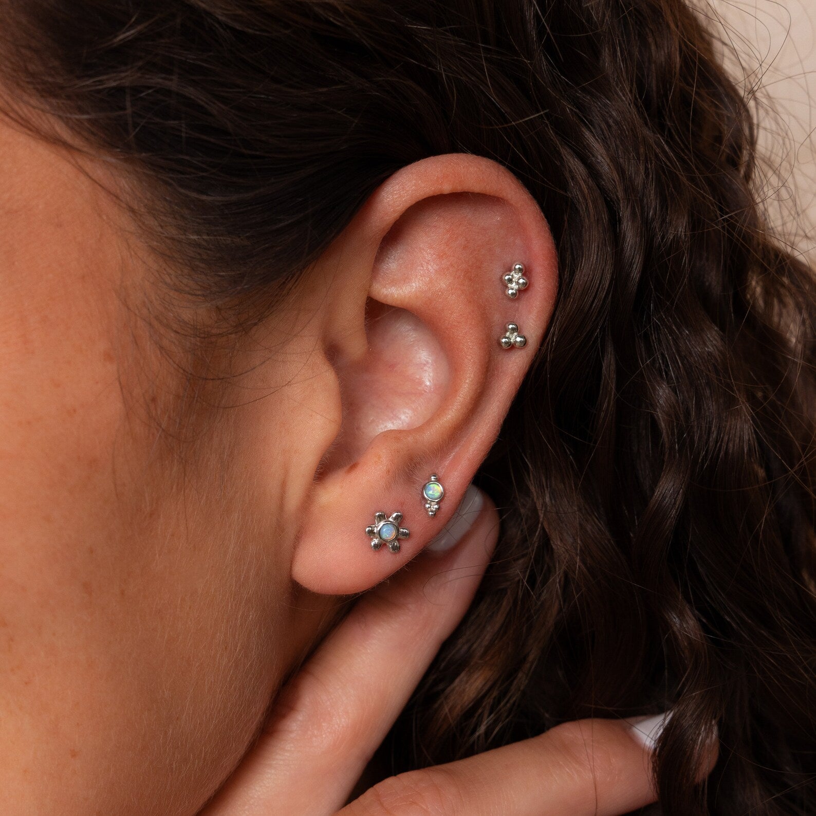 Close-up of a woman's ear adorned with the Opal Cluster Studs Set in her cartilage piercings, featuring sparkling opal and silver clusters, as she gently touches her ear.