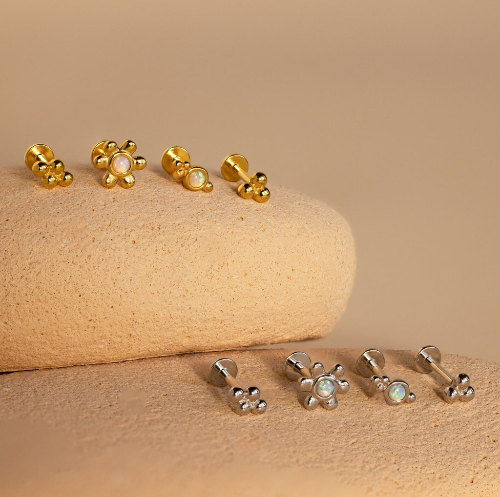 The Opal Cluster Studs Set features six pairs of gold and silver stud earrings with opal centers, perfect for cartilage piercings and beautifully presented on textured stones.