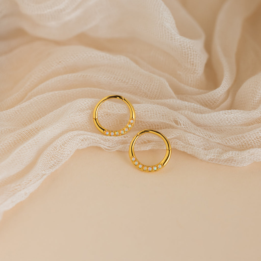 Opal Cartilage Huggies shown on soft cream fabric—these gold hoops with petite white opals offer a minimalist style and subtle elegance for any look.