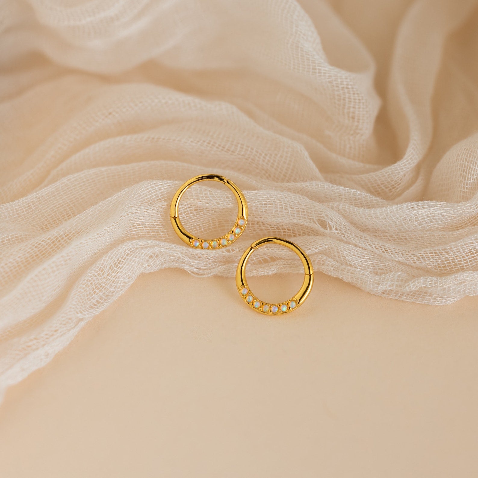 Opal Cartilage Huggies shown on soft cream fabric—these gold hoops with petite white opals offer a minimalist style and subtle elegance for any look.