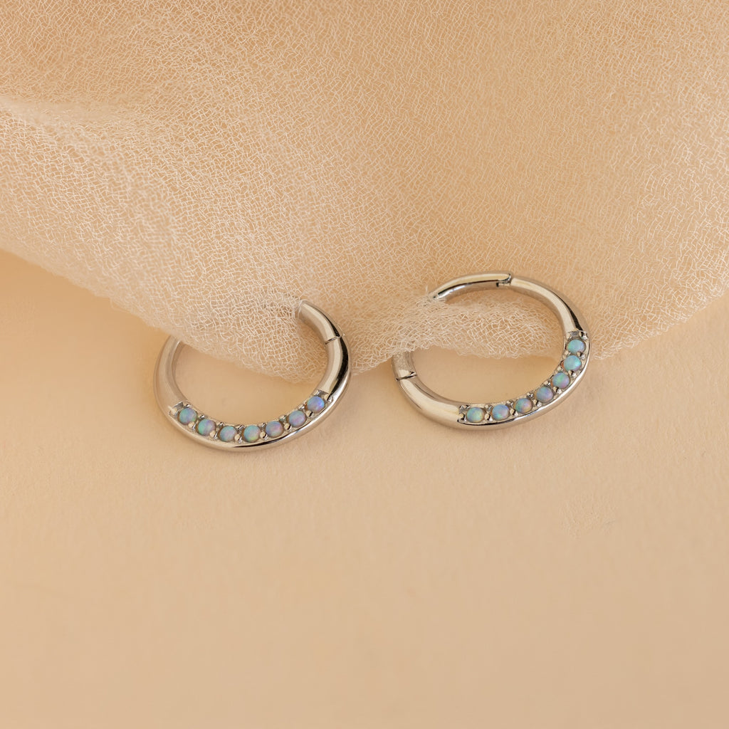 Opal Cartilage Huggies—silver hoop earrings with petite blue opals, ideal for minimalist style or as a chic helix piercing, displayed on a soft beige fabric background.