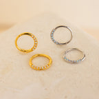 Two gold and two silver Opal Cartilage Huggies with small embedded stones, ideal for helix piercings, displayed on a light textured surface.