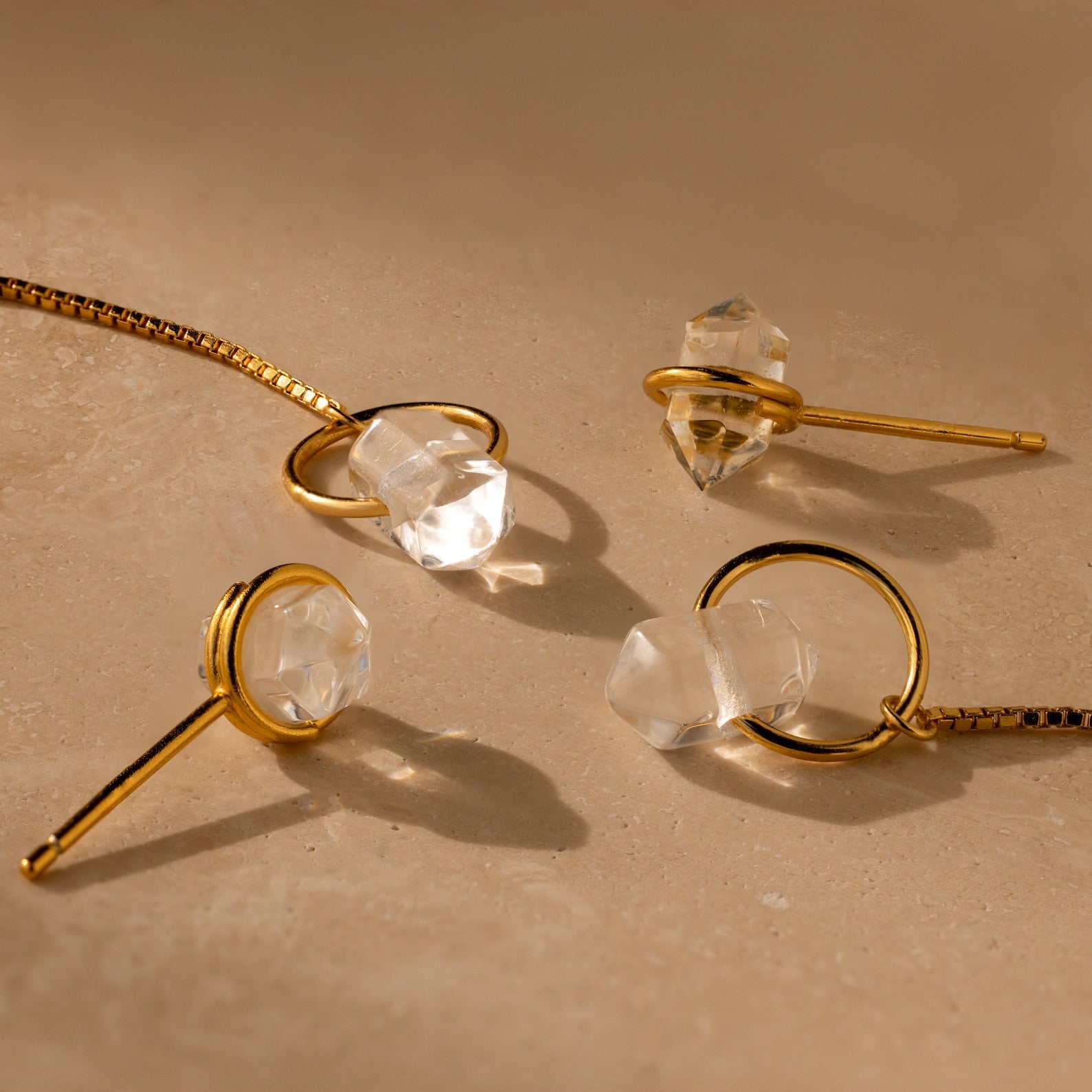 Herkimer Diamond Threader Earrings with clear crystal stones in gold, displayed on a beige surface.