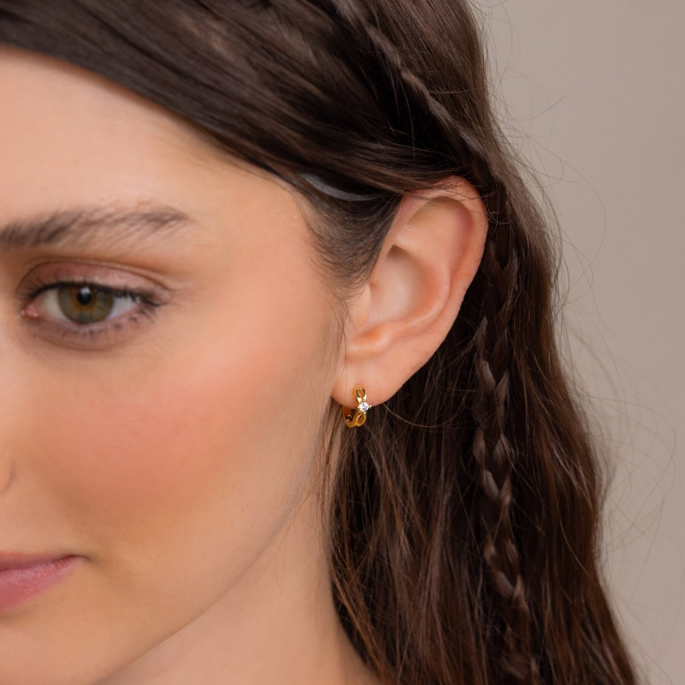 A woman with brown braided hair wears dainty Diamond Infinity Hoops, shown in a close-up side view.