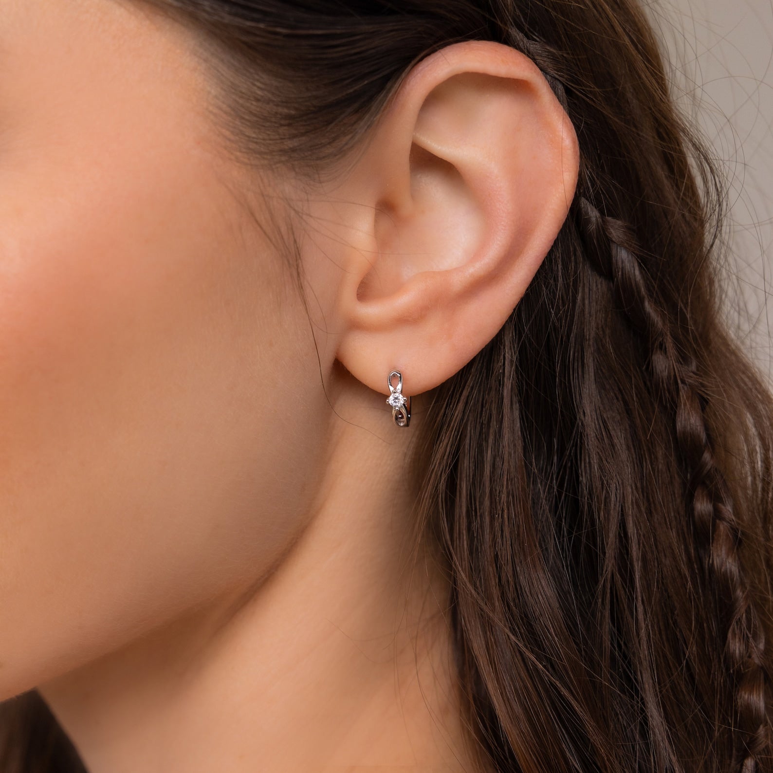 Close-up of a woman's ear wearing Diamond Infinity Hoops; her brown hair is styled with a delicate, thin braid, adding a romantic touch to the elegant jewelry.