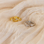 Diamond Infinity Hoops—elegant gold and silver earrings with sparkling diamonds in a romantic infinity design—are displayed on soft beige fabric.