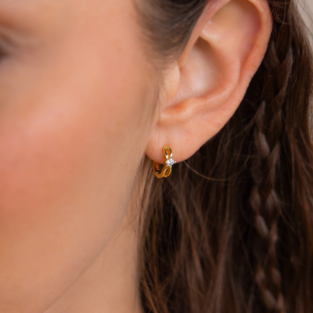 Close-up of a woman’s ear wearing a small gold Diamond Infinity Hoop with a single clear gemstone.