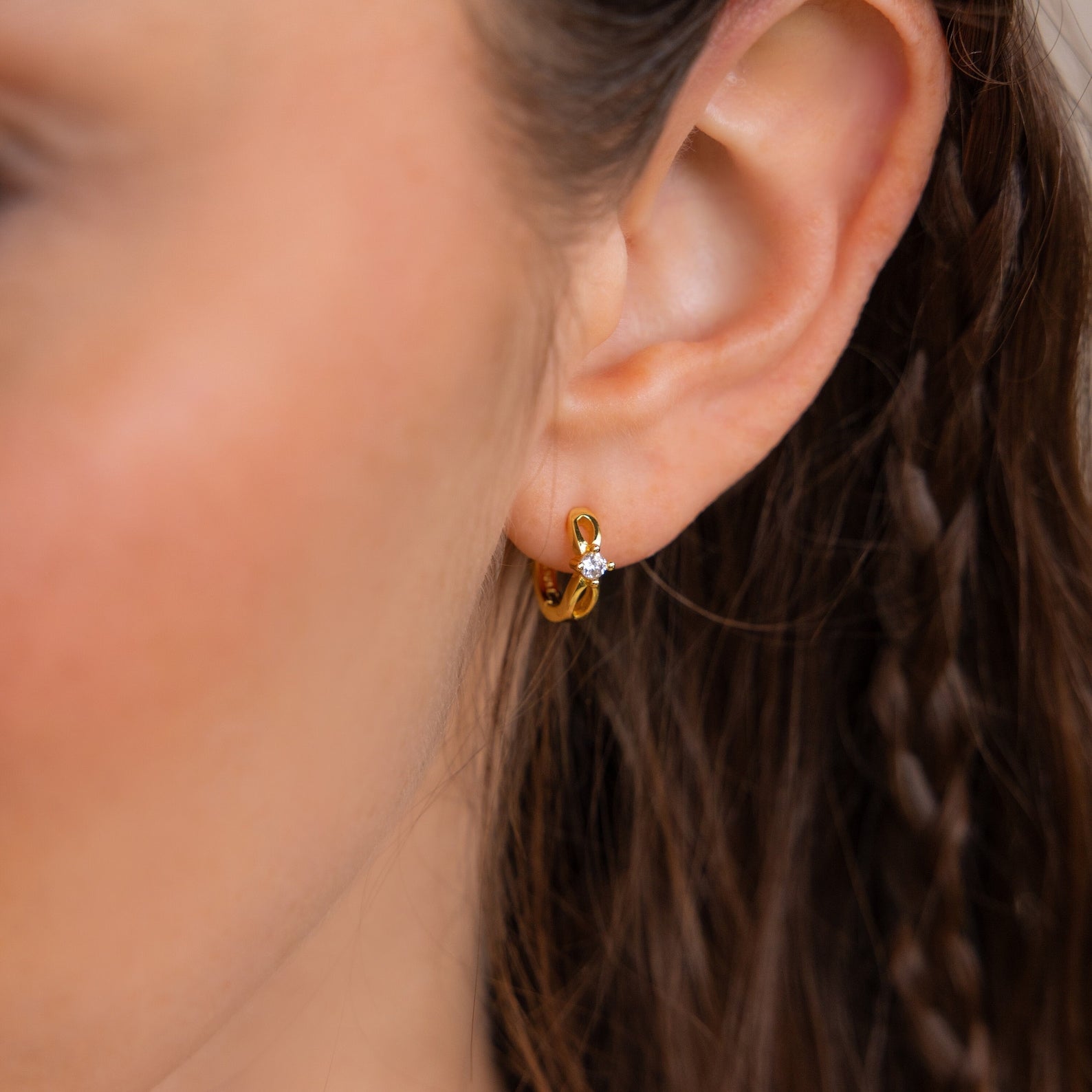 Close-up of a woman’s ear wearing a small gold Diamond Infinity Hoop with a single clear gemstone.