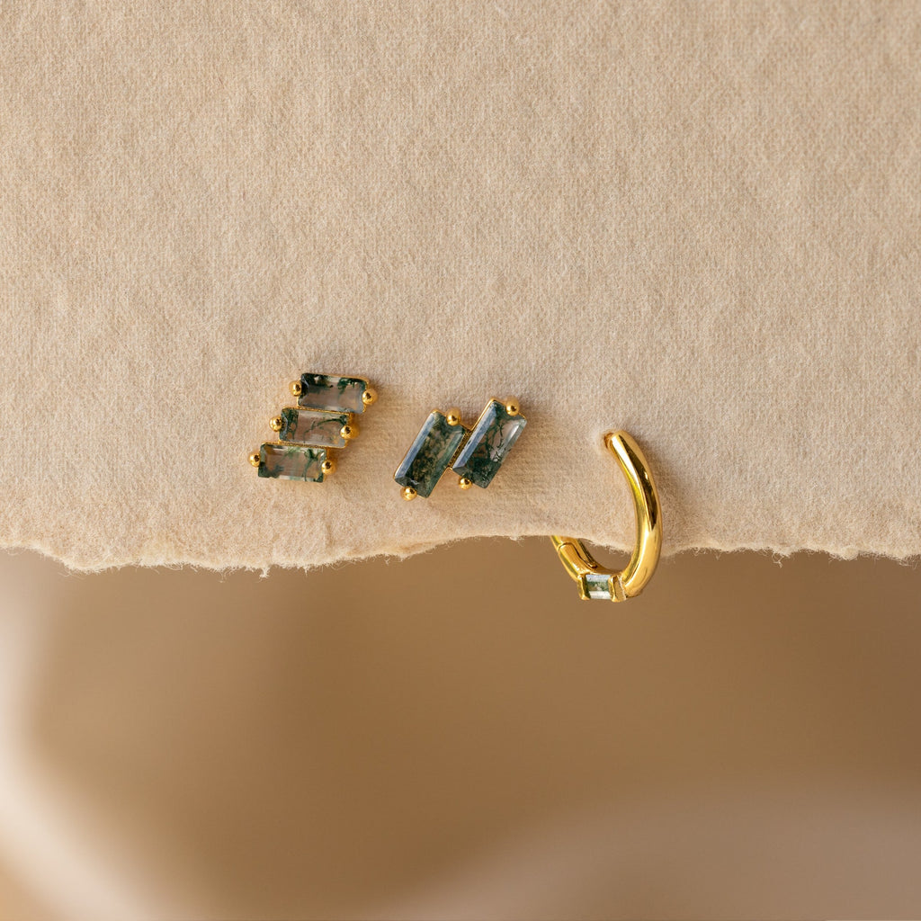 The Agate Cartilage Earrings Set features three gold agate earrings with green gemstones on a textured beige surface—ideal for gifting to friends or adding style to your cartilage piercings.
