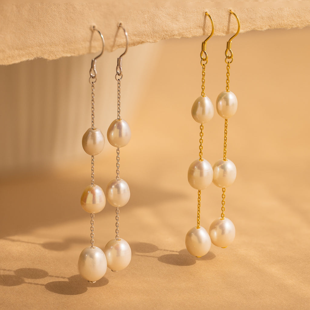 Close-up of two Long Pearl Dangle Earrings in Gold and Silver. 