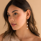 Model wearing long gold pearl chain earrings.