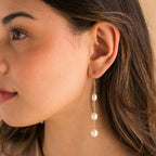 Close-up of model wearing long gold pearl chain earrings.