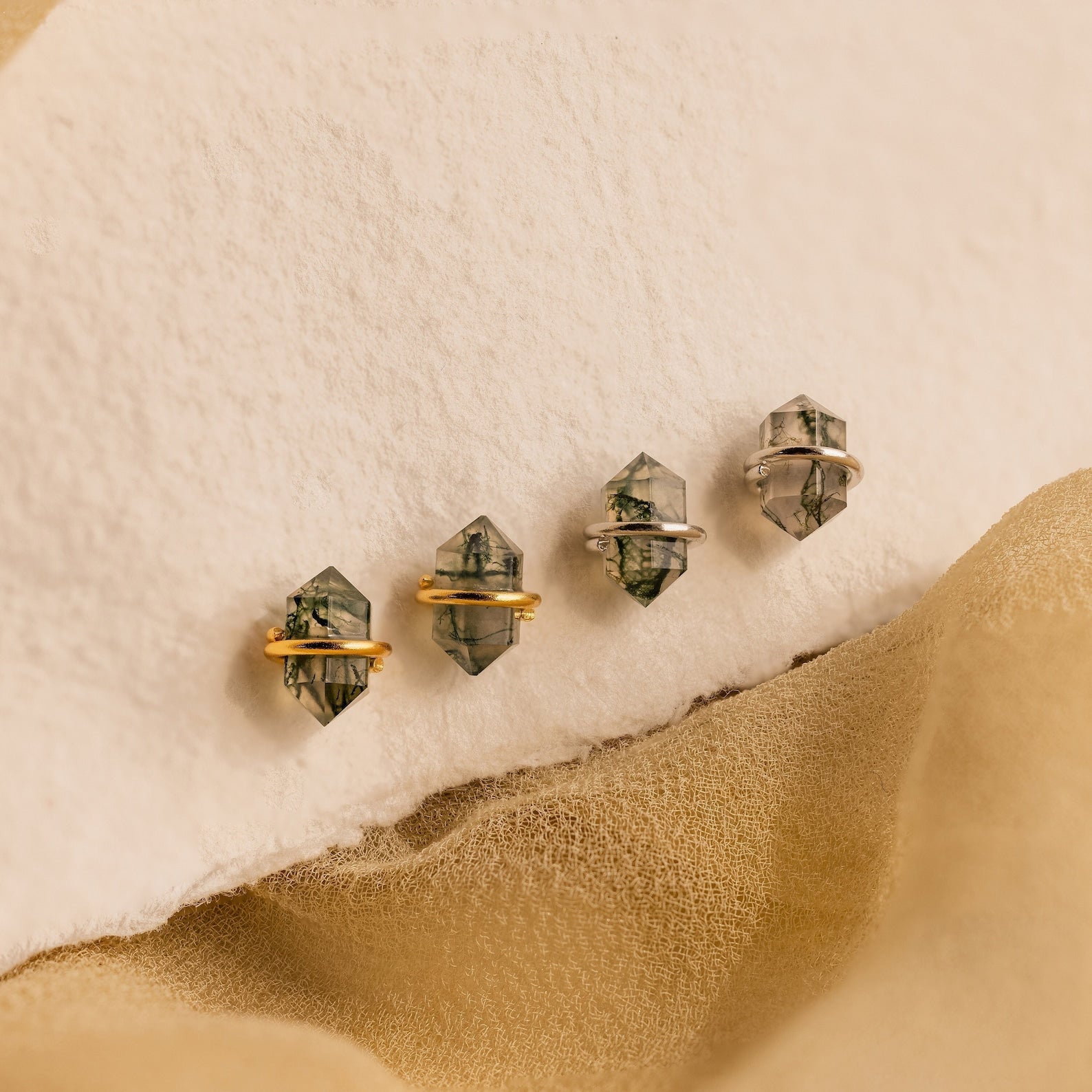 Four crystal rings with gold and silver bands rest on a soft beige surface, beautifully paired with Herkimer Agate Studs and geometric gemstone earrings for a chic, coordinated look.