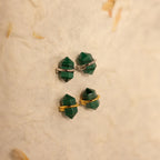 The Herkimer Malachite Studs feature geometric green malachite stones with gold and silver bands, displayed on a textured beige surface.