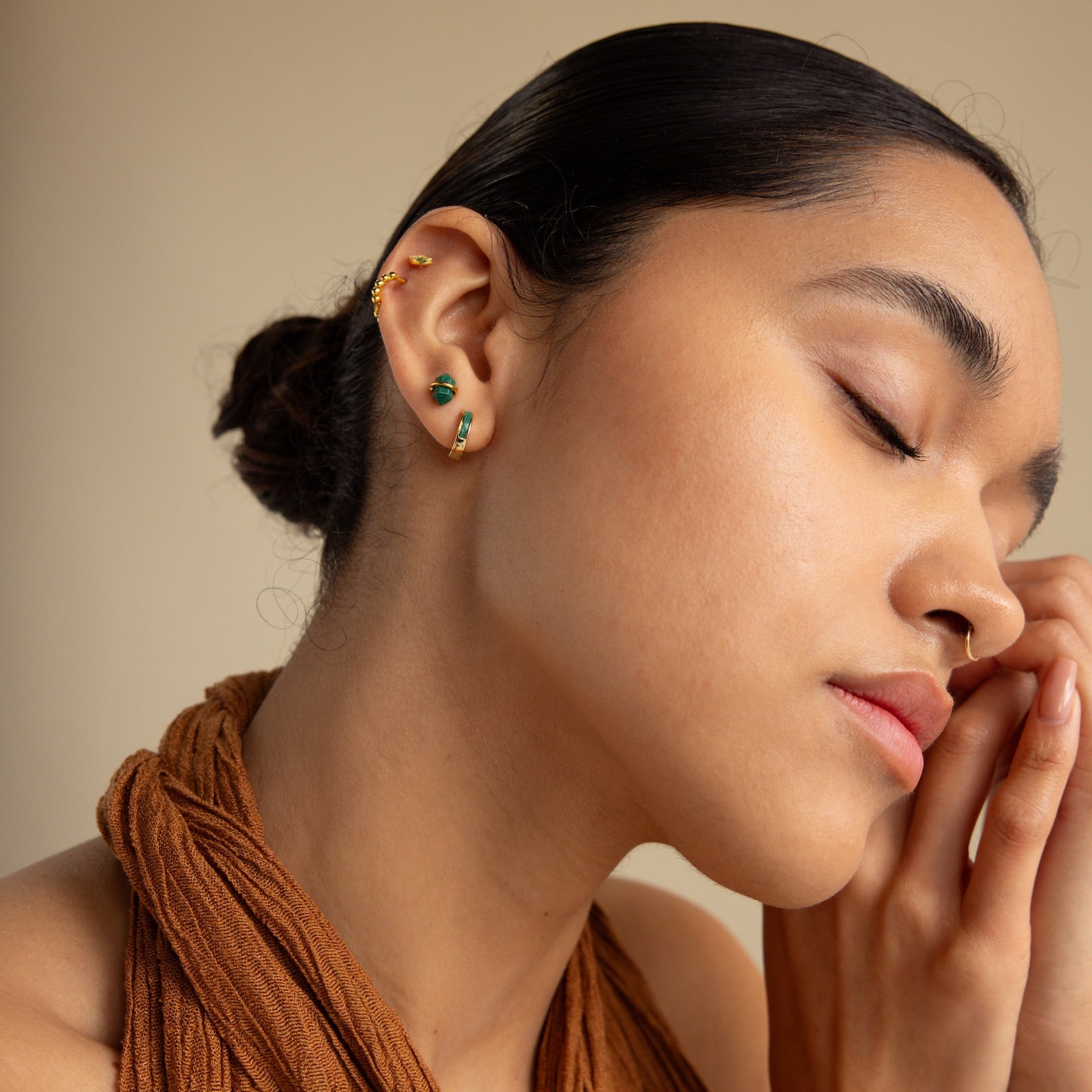 Woman with closed eyes, wearing Herkimer Malachite Studs and a brown halter top, gently rests her face on her hands.