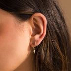 Close-up of a woman's ear wearing Mother of Pearl Inlay Huggies—gold hoops, one adorned with a small dangling pearl.